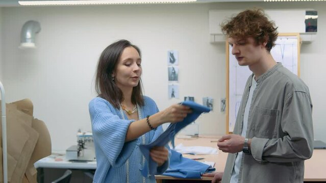 4K. A young woman seamstress works with a client in a sewing workshop, she takes measurements with a measuring tape