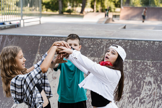 Stack of children hands. Concept of friendship sports support of children. Kids with skateboards and penny boards posing together on sport ramp on skate board playground.