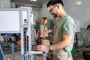 Male brewer working in a brewery filling bottles with beer.