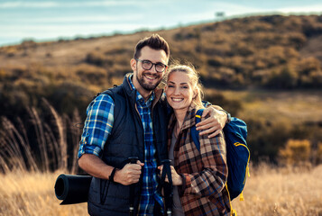 Portrait of couple with backpacks hiking together in nature on autumn day.