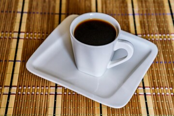 Black coffee in a white cup on a napkin-mat on the table close-up.