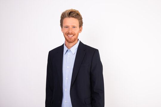 Portrait of young happy Caucasian businessman standing and smiling at camera. Bearded man wearing blue shirt and black suit coat with positive expression. Successful businessman concept