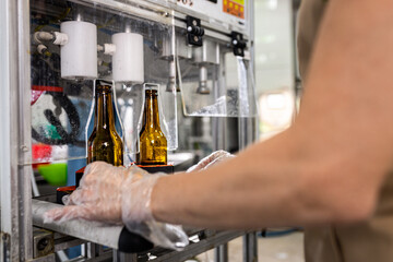 Close up of male brewer hands in a brewery filling bottles with beer.