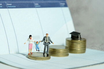 Miniature people toy figure photography. Couple with baby child walking above coin money stair to...