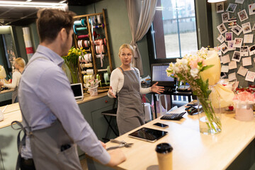 two employees of a flower shop talking to each other standing in front of a desk