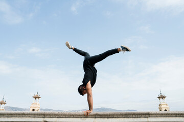 Latin boy doing the vertical on a stone railing in front of the views of Barcelona on a sunny day....