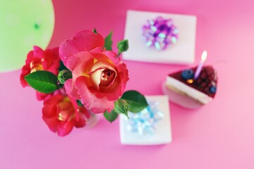 Dessert with white cream decorated with fresh berries and a burning candle, fresh roses, balloons and gifts on the table, happy birthday, holiday, congratulation, postcard