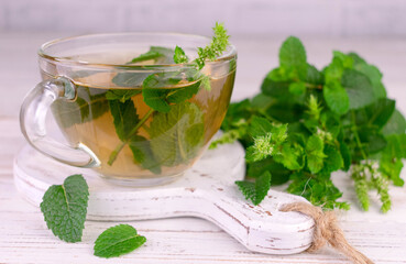 Mint tea in a transparent cup on a white wooden board.Close-up.
