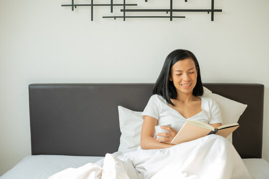 Woman reading book with cup of coffee at home in the living room. Morning book reading. rest, comfort, leisure and people concept - close up of young woman reading book in bed at home bedroom