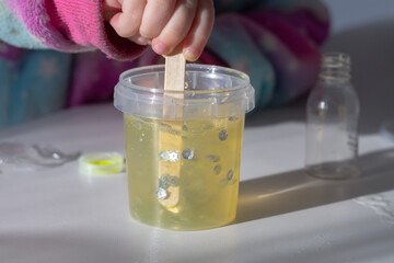 Children make slime themselves from glue and thickener, kids play with homemade yellow slime