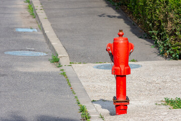 Red hydrant on the sidewalk next to sewer cap or manhole cover
