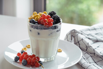 Yogurt, breakfast loops oat cereal, and fresh summer berries fruits in glass on white table