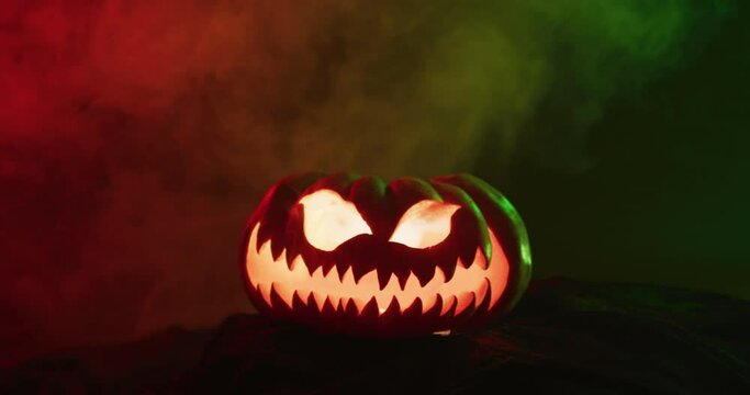 Video of halloween carved pumpkin with smoke and green and red light on black background