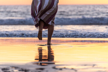 Rear View of Woman Legs Walking on a Beach to the Ocean at Sunset Time.Copy Space