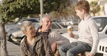 Smiling, happy and loving grandparents and grandson eating ice cream on a fun day. Mature couple and child smiling and talking together. Cute family group enjoying the sunshine and relaxing outdoors - Powered by Adobe