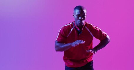 African american male rugby player catching rugby ball over pink lighting