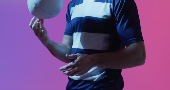 Caucasian male rugby player with rugby ball over pink lighting