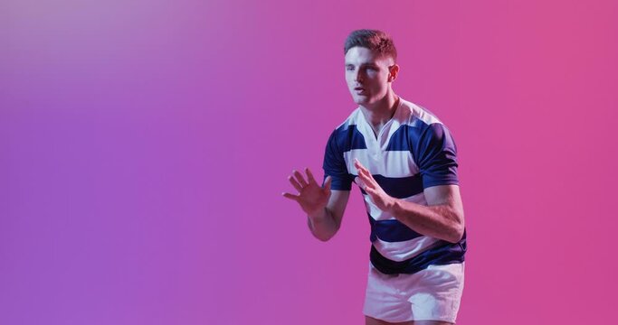 Caucasian male rugby player catching rugby ball over pink lighting