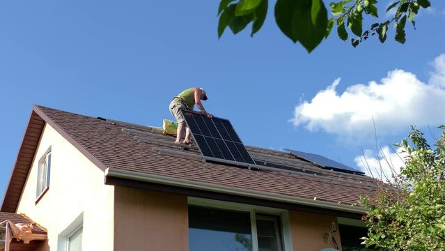 Man instals solar panel on on bituminous tiles roof
