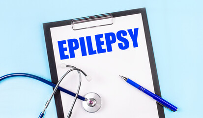On a blue background, a stethoscope, a pen and a tablet with paper and the text EPILEPSY. Medical...