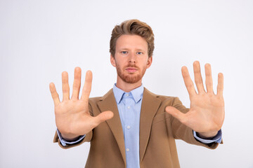 Portrait of serious young businessman making stop gesture. Caucasian bearded man wearing blue shirt and beige woolen suit coat standing with refusal gesture. Forbiddance concept
