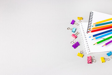 Notebooks, colored pencils and paper clips on a light gray table. Place to copy. Banner