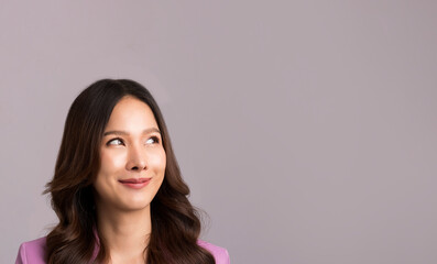 Asian woman long hair, wearing a pink suit is smiling and looking at the gray empty background.