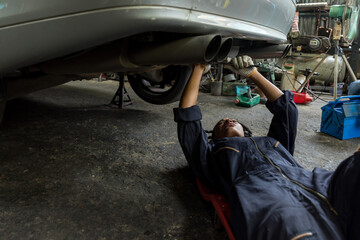 Mechanic lying down and working under car at auto service garage. Technician vehicle maintenance...