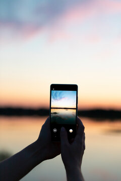 Woman's hands with mobile phone taking photos of beautiful sunset close up 