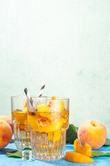 Homemade peach ice tea with ripe fresh peaches on high-colored blue wooden background