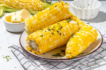 Boiled corn with butter and herbs. Ripe yellow organic cooked corn cobs, on a white kitchen table