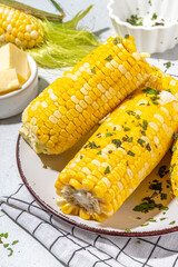 Boiled corn with butter and herbs. Ripe yellow organic cooked corn cobs, on a white kitchen table