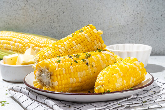 Boiled corn with butter and herbs. Ripe yellow organic cooked corn cobs, on a white kitchen table