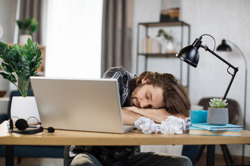 Young frustrated exhausted man laid his head down on the table sitting at desk with pc laptop. Achievement business career concept. Overworked and tired businessman sleeping at work in his office.