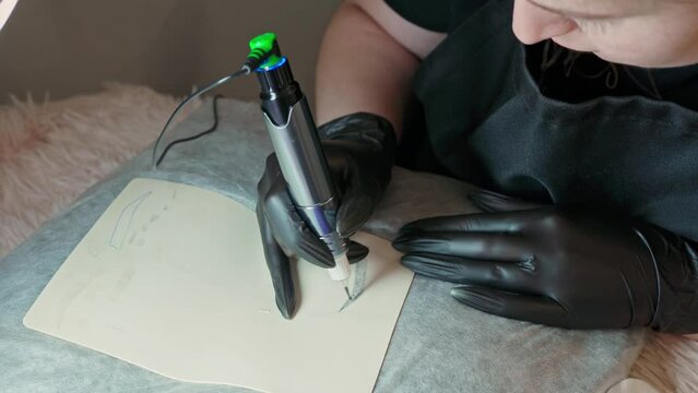 female hands in black gloves close-up draw an eyebrow on a silicone mat with a tattoo machine. eyebrow tattoo, eyebrow makeup, apprentice, training