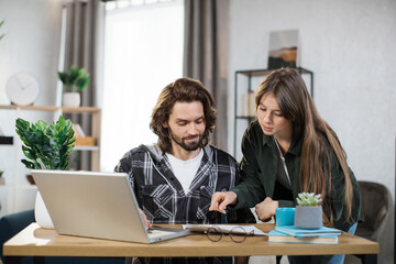 Male and female business partners in casual wear discussing common project at bright office. Caucasian colleagues using modern gadgets for work.