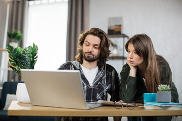 Young man and woman in casual outfit looking at computer screen during working meeting. Young business partners cooperating at bright office.