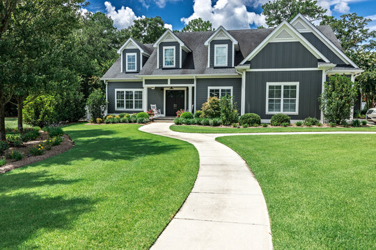 A large gray craftsman new construction house with a landscaped yard and a long leading walkway to the front door