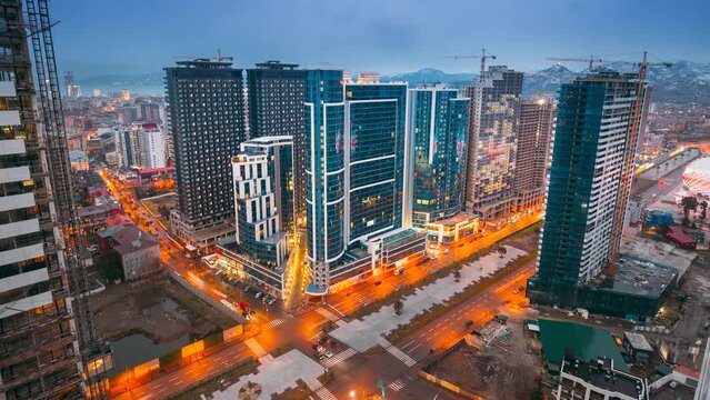District Street Night Time Lapse. City Traffic and highrise houses . Street Night Yellow Illumination reflected in Skyscrapers windows. Evening Night City Traffic. Night View Scenic Of Skyscraper