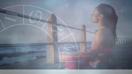 Animation of zodiac signs with young african woman meditating on pier at beach - Powered by Adobe