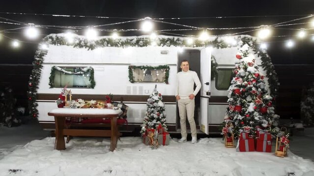 Happy young couple hugs and smiles and snow falls near christmas trees at the eve of new year celebration in winter day. Smiley man and woman wearing white pullovers love each other