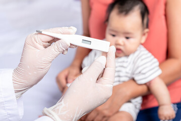 Close-up images, Doctor's hand holding a thermometer for measuring children's temperature, with blur background of mother is holding baby newborn is 3 montsh old, to baby newborn and influenza concept