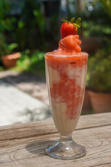fresh and cool strawberry yogurt smoothie in a tall glass cup on wooden table, blur nature background, food, fruit, copy space