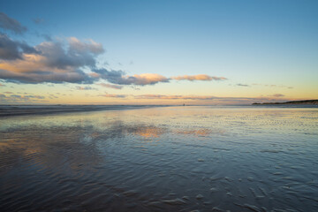 Sunset on a beach with reflections on wet sand and distant figures.