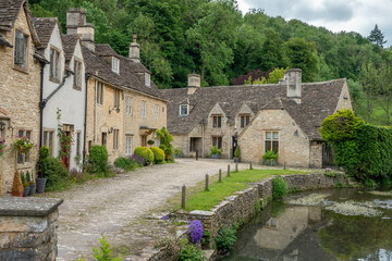 honey coloured Cotswold stone houses alongside By Brook in Castle Combe Wiltshire England often...