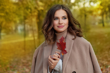 Portrait of a beautiful young happy woman enjoying autumn in the park. Fall season and cute walking lady, romantic portrait