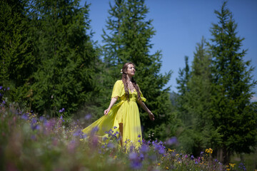 Obraz na płótnie Canvas A girl in a yellow dress walks in a flowering field. The field blooms in the mountains