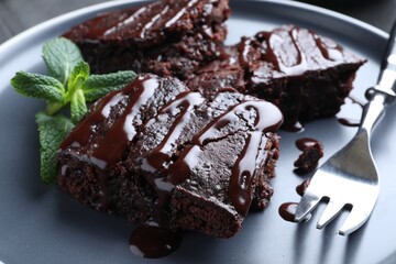 Delicious chocolate brownies with sweet syrup and mint on plate, closeup