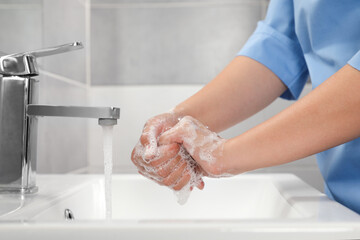Doctor washing hands with water from tap in bathroom, closeup - Powered by Adobe