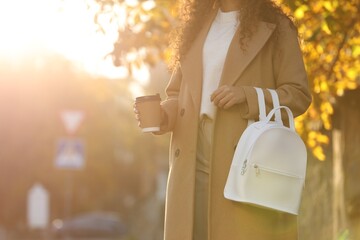 African-American woman with stylish white backpack and hot drink outdoors on sunny day, closeup....